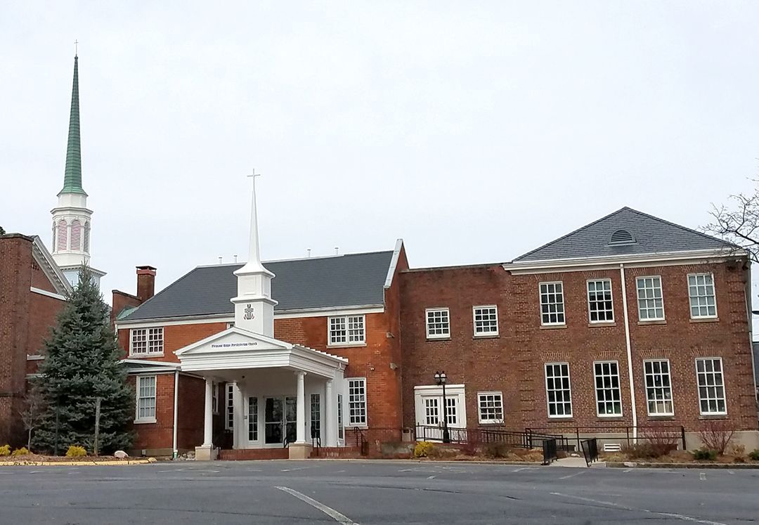Brick church building with a steeple and covered entrance under an overcast sky.