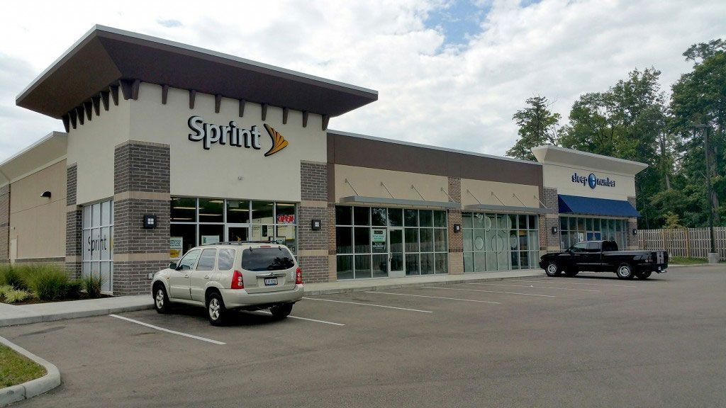 Sprint store and other businesses in a strip mall, SUV parked in front.