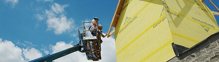 Construction worker in a lift working on a yellow building under a blue sky.