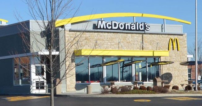 McDonald's restaurant with a yellow arch, sign, and building trim against a blue sky.