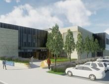 Modern building with parking lot and trees. Person walking toward entrance. Blue sky in background.