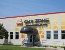 Sky Zone trampoline park entrance, beige building with black awning and signage.
