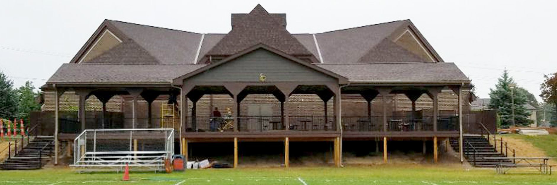 Brown building with a wraparound porch and steps leading to a grassy field.
