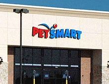 PetSmart store front, red and blue logo above dark glass doors. Beige facade, under a bright blue sky.