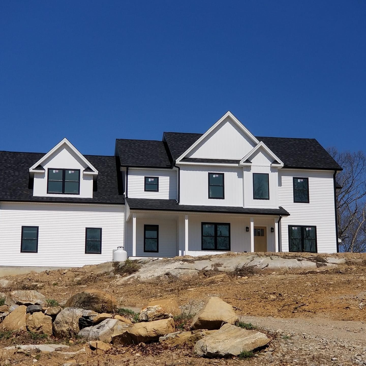a white house with a black roof sits on top of a dirt hill