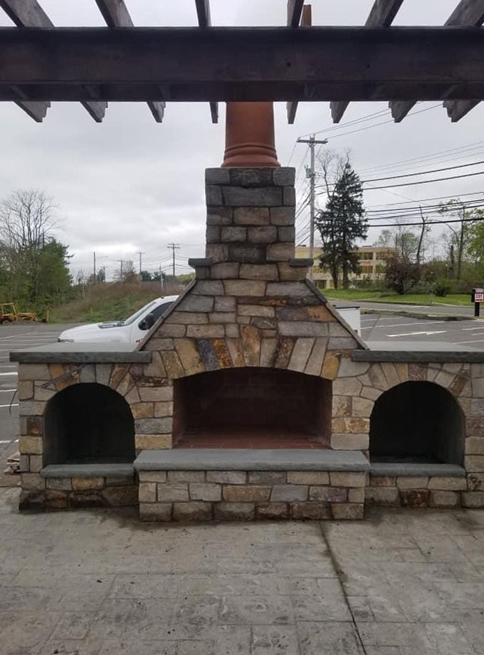 a stone fireplace is sitting under a pergola in a parking lot