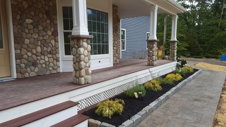 the front porch of a house with a stone wall and pillars