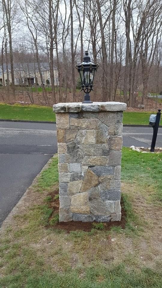a stone pillar with a lamp on top of it next to a mailbox