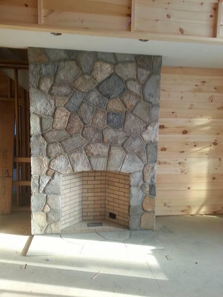 a stone fireplace in a living room with wooden walls