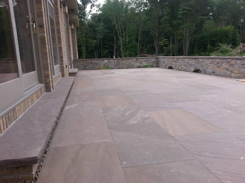 a large patio with a stone wall and trees in the background