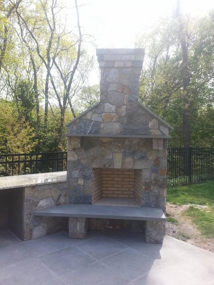 a stone fireplace with a bench and a fence in the background