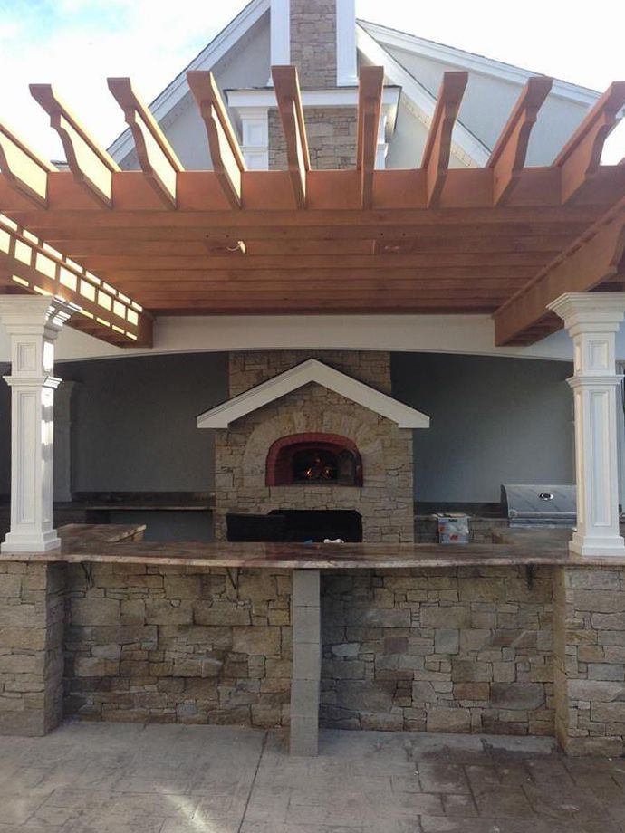 a brick oven under a wooden pergola in front of a house