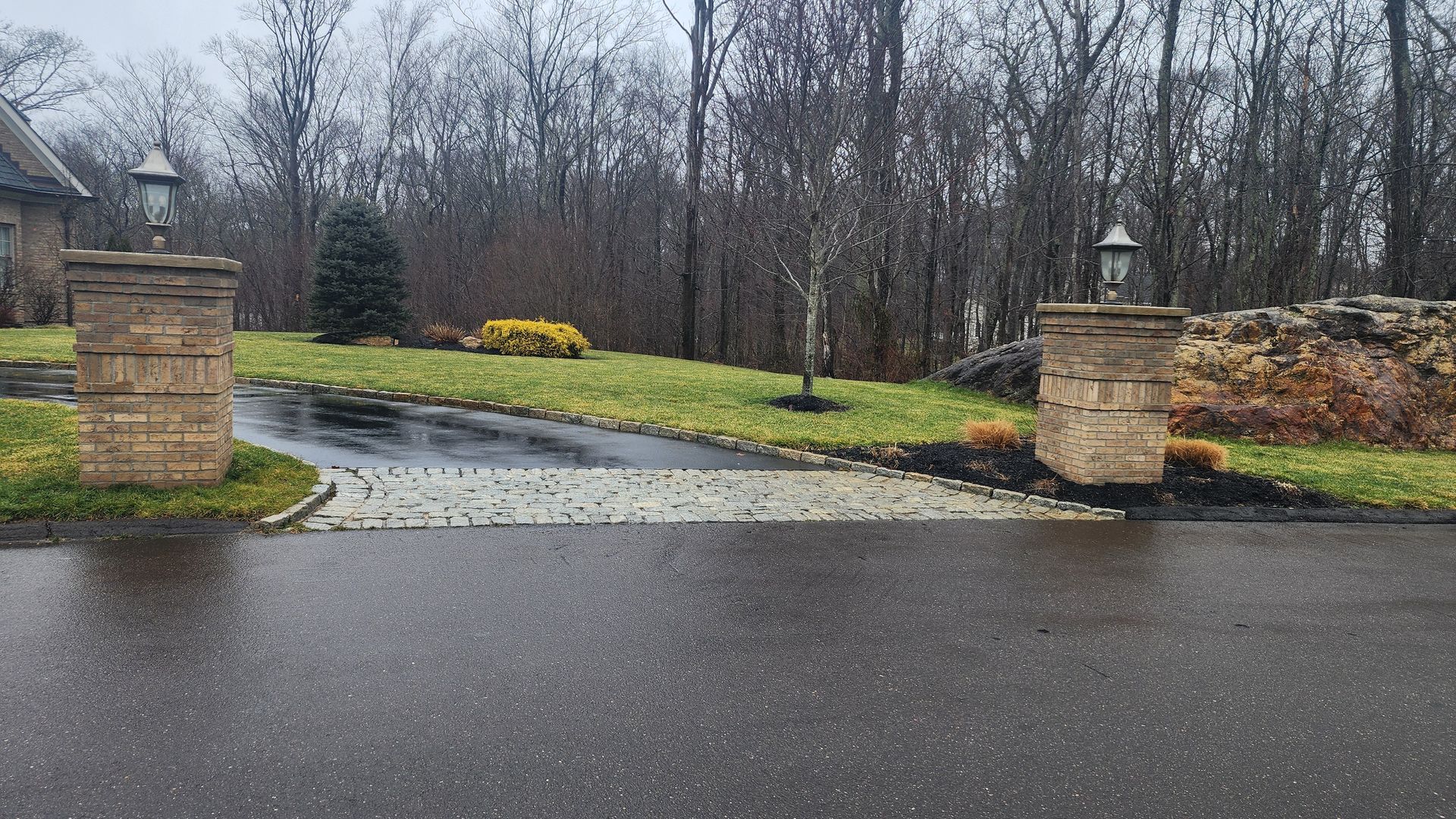 a driveway with two stone pillars leading to a house on a rainy day