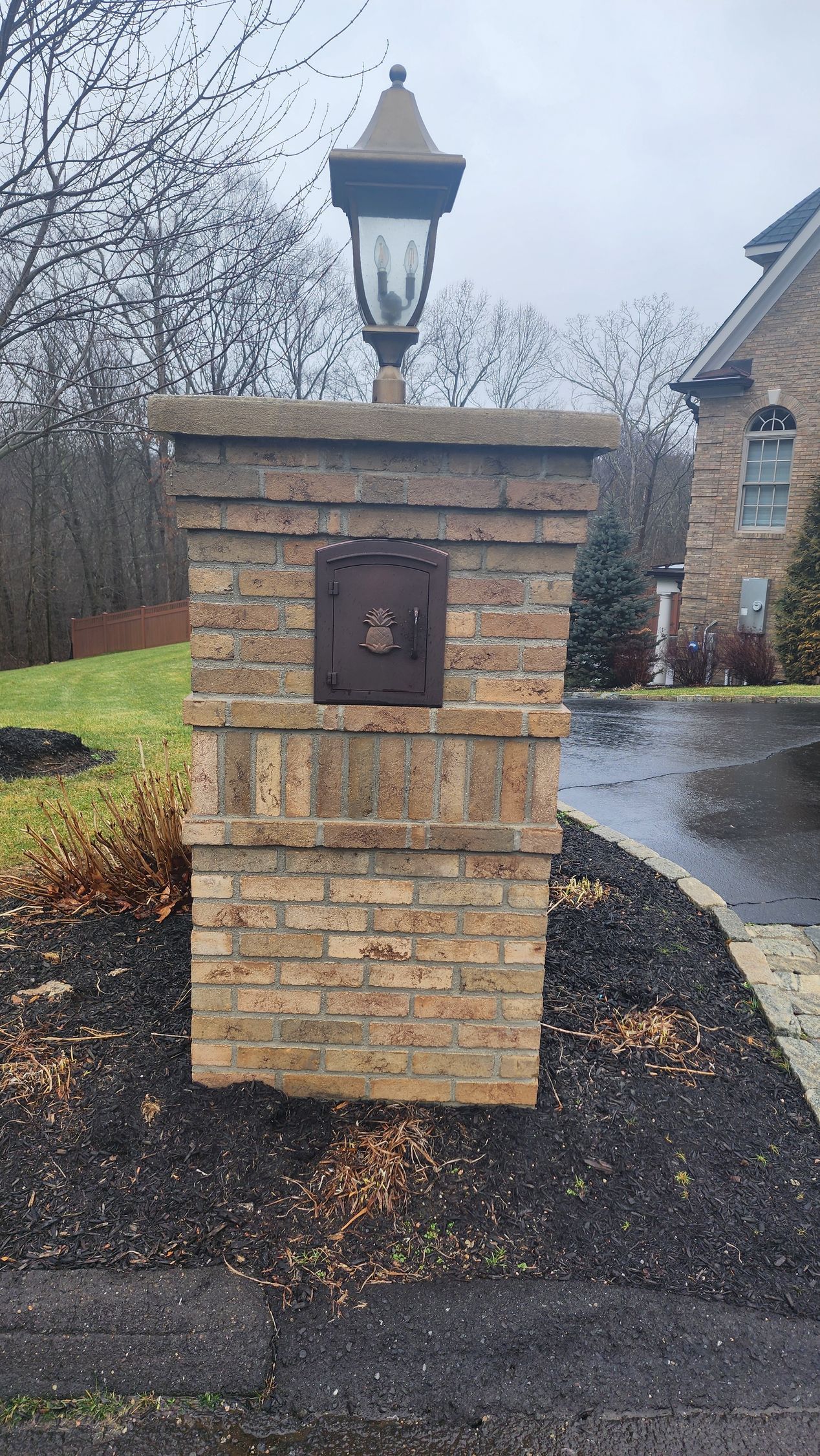 a brick pillar with a mailbox and a lamp on top of it
