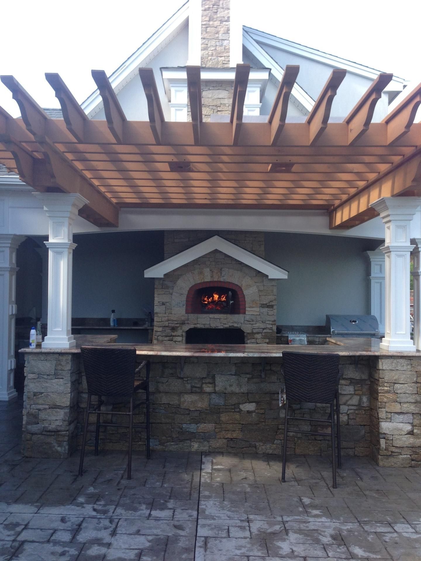 an outdoor kitchen with a pizza oven under a pergola