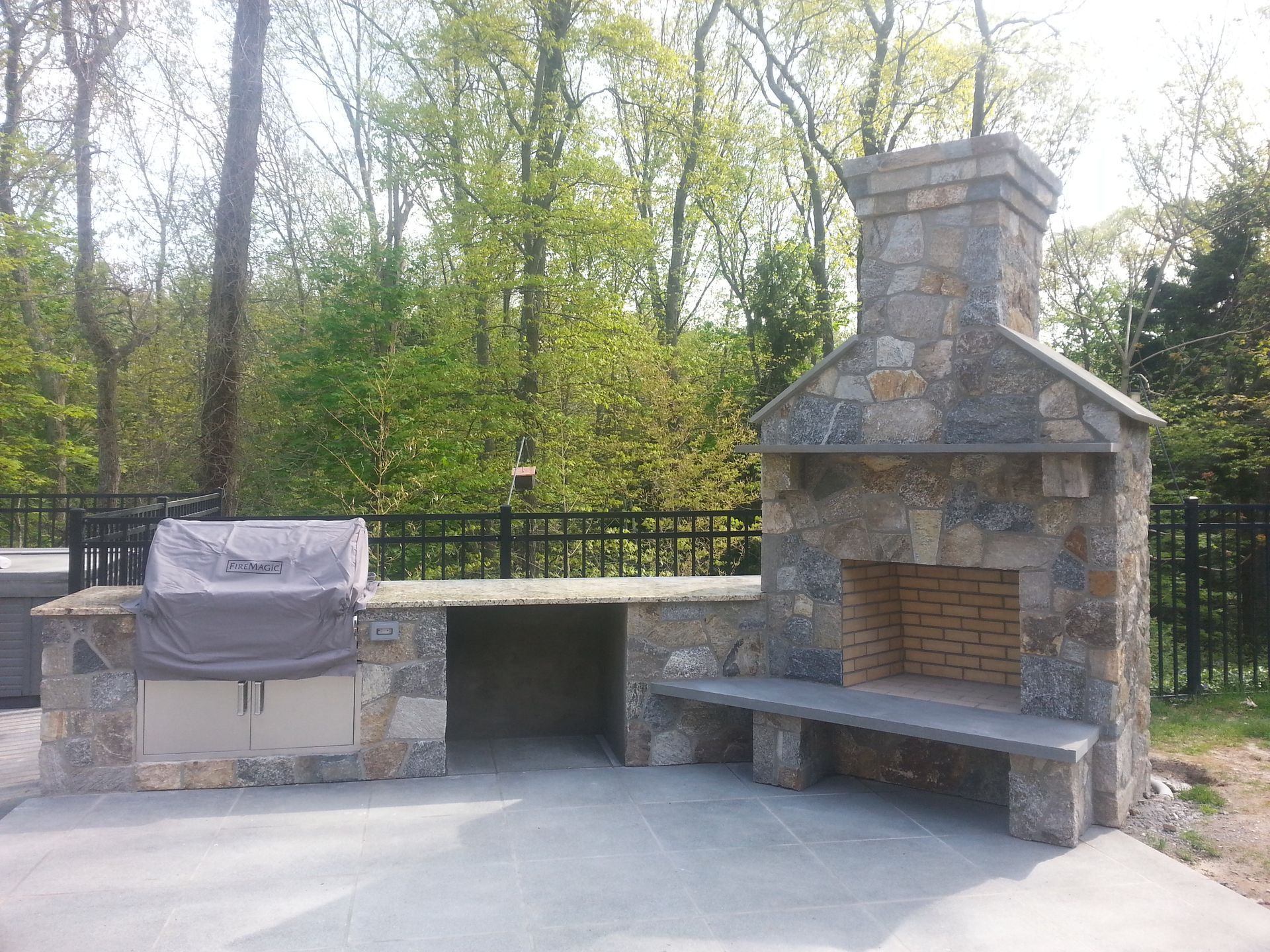 a stone fireplace with a grill and a bench in a backyard