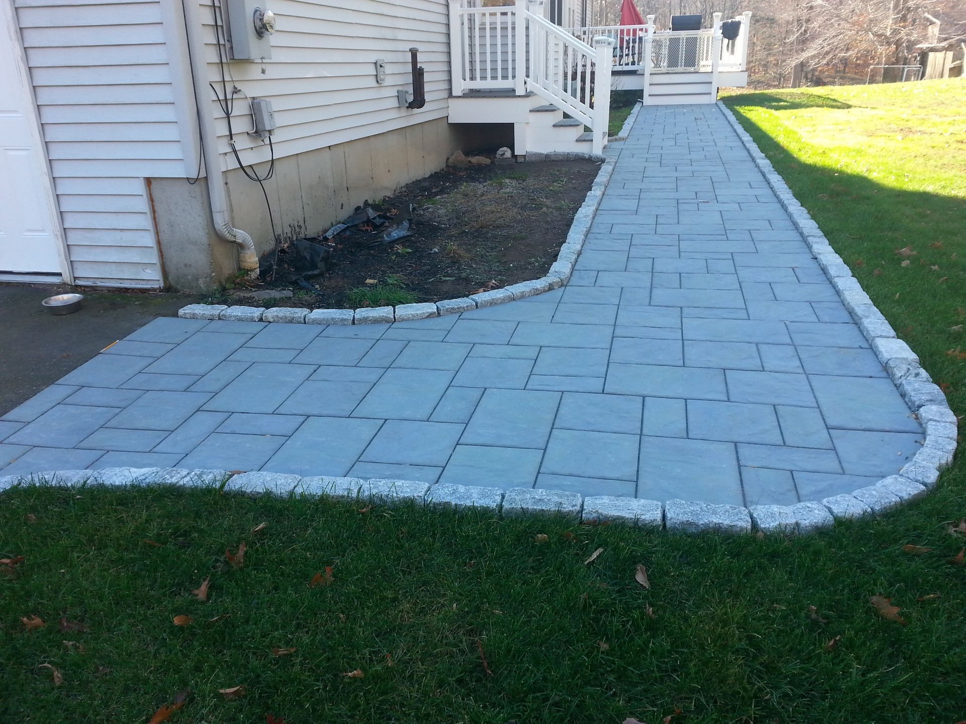 a brick walkway leading to a house with a white house in the background