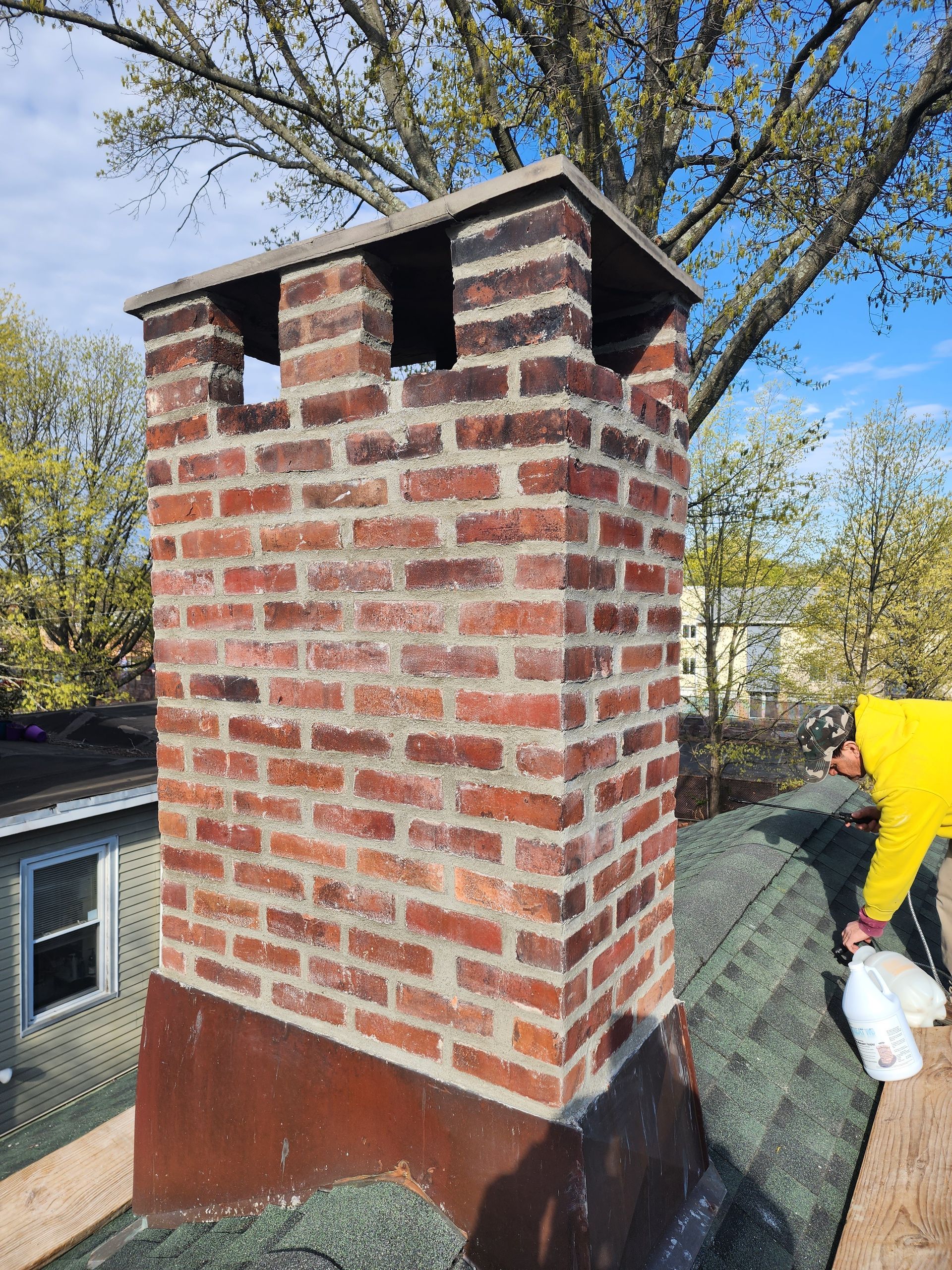 a man is working on a brick chimney on the roof of a house