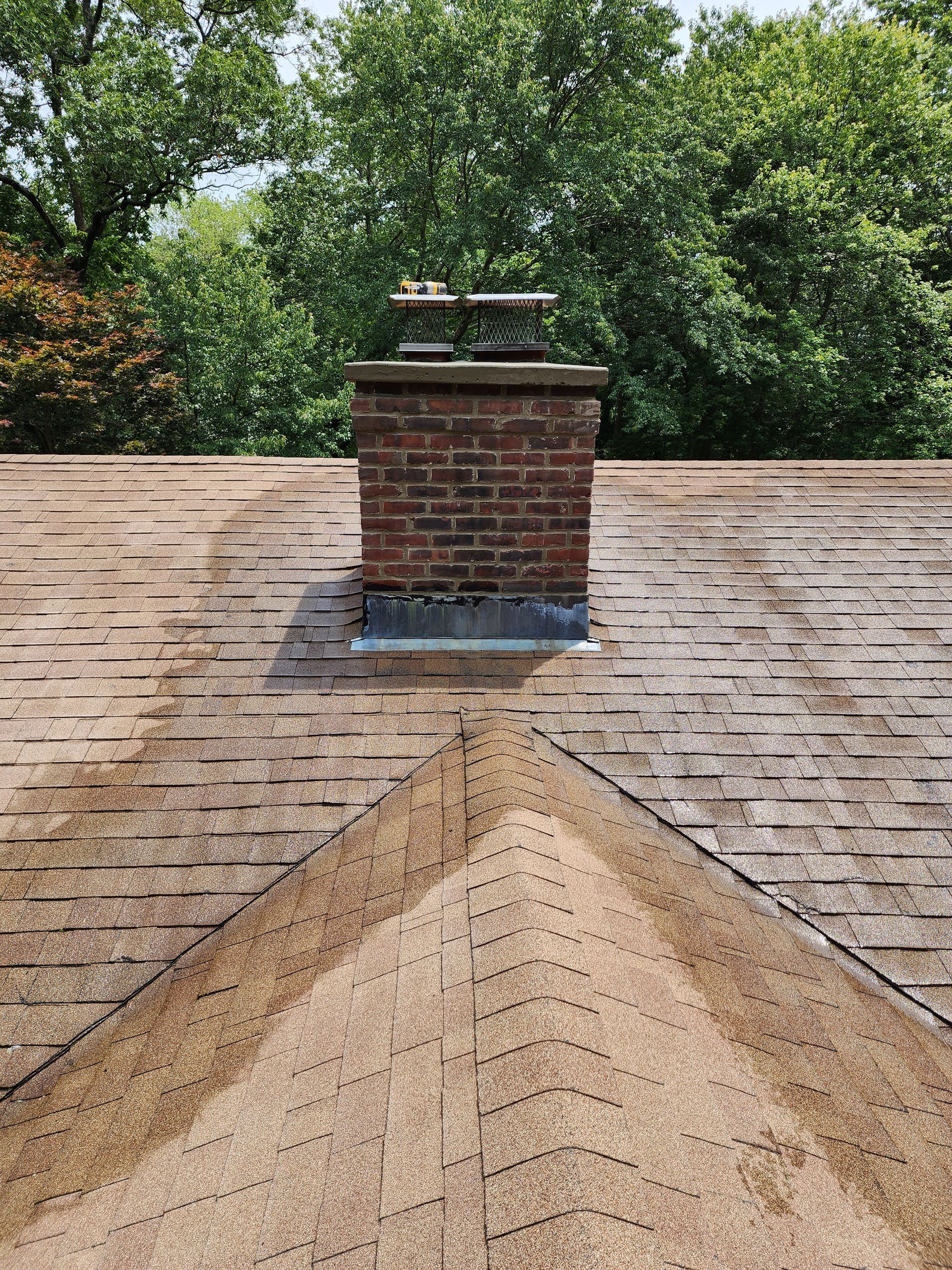 a brick chimney on top of a roof with trees in the background