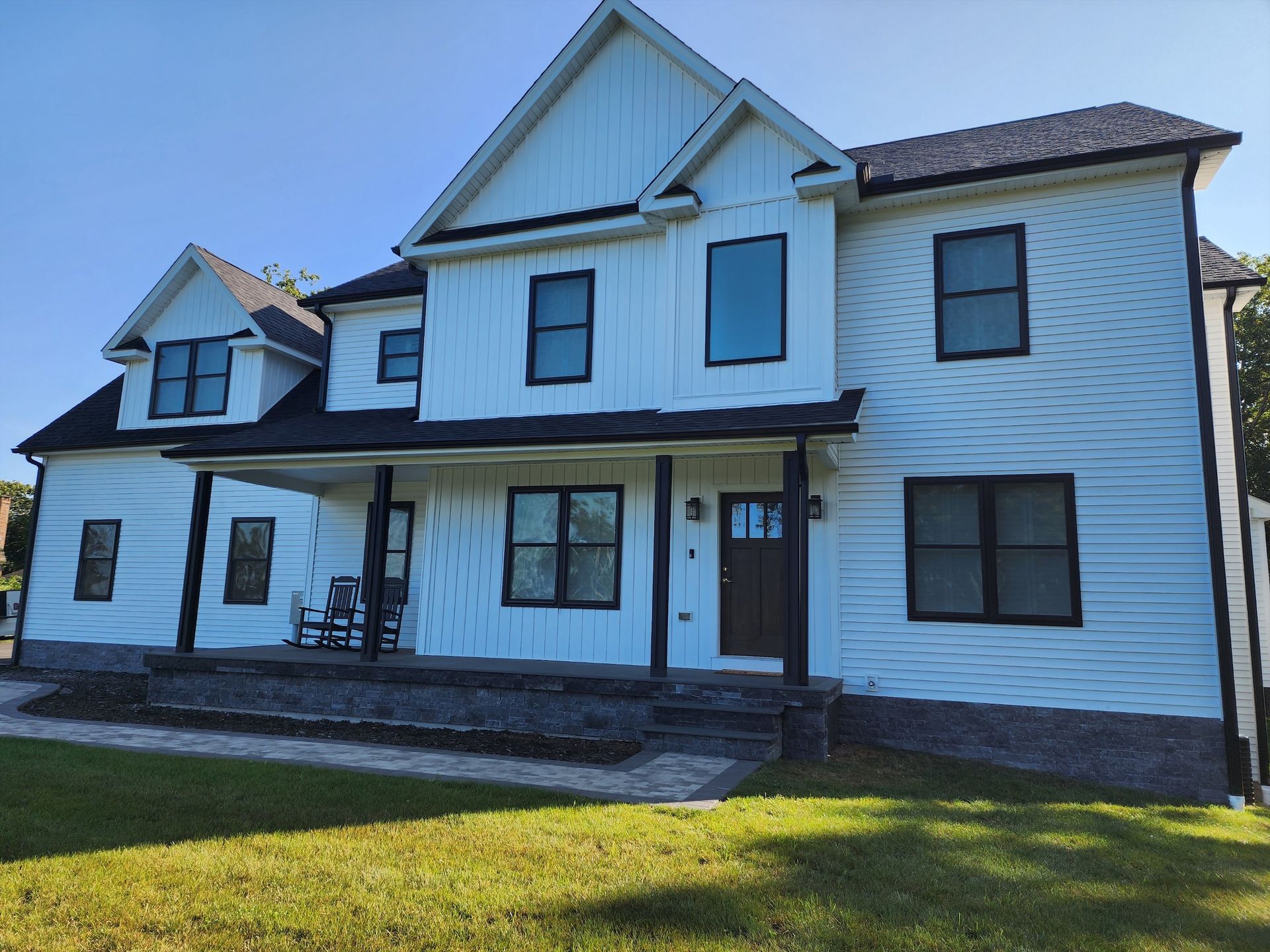 a large white house with a black roof is sitting on top of a lush green field