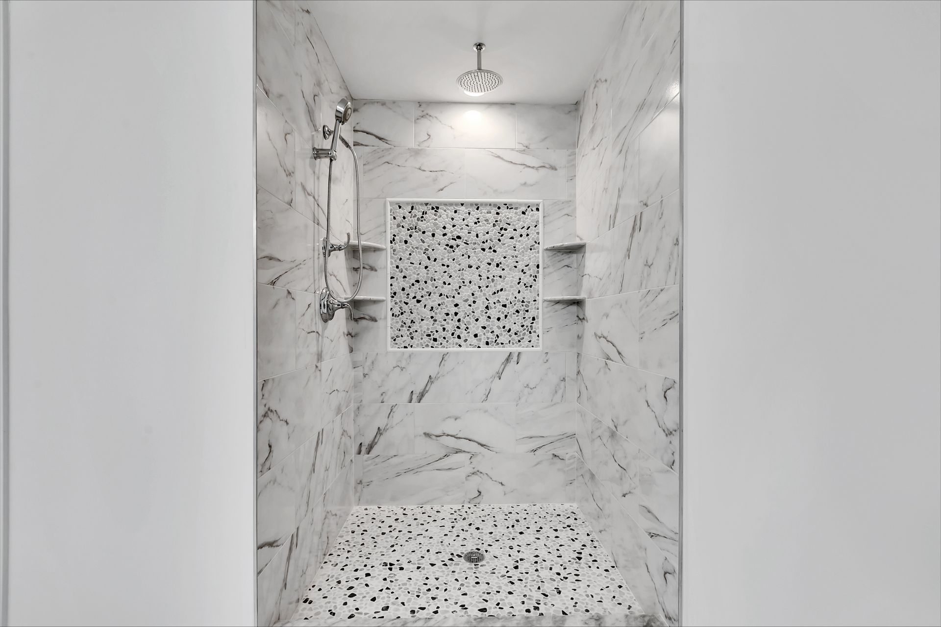 a walk in shower with marble walls and a tiled floor