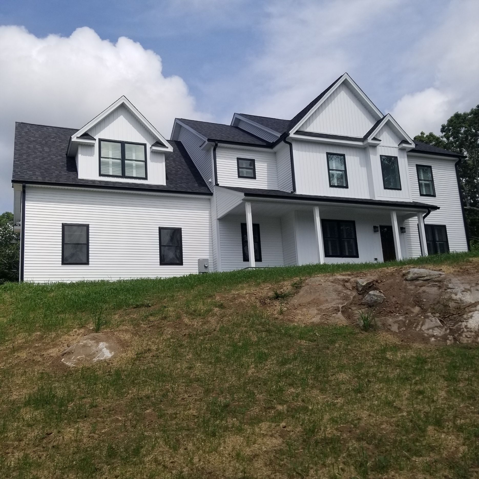a large white house with a black roof is sitting on top of a grassy hill