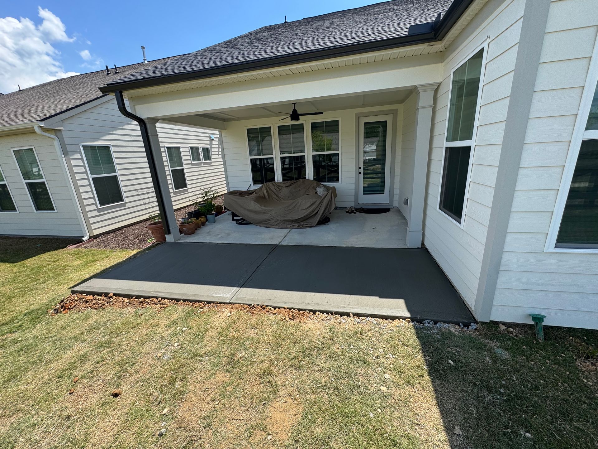 Covered backyard patio with white siding, dark roof, and a grill under a gray cover next to a lawn.