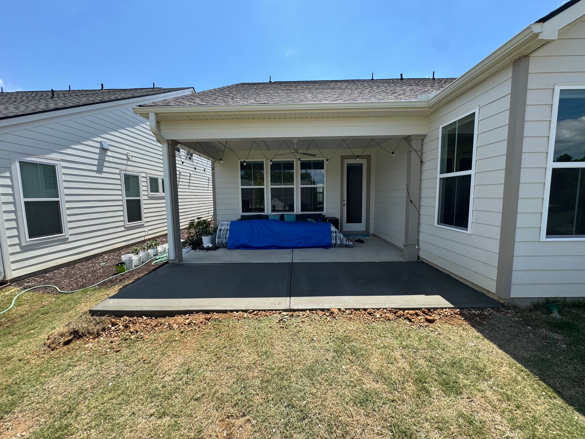 Covered patio with blue seating and a concrete porch in a backyard between two houses