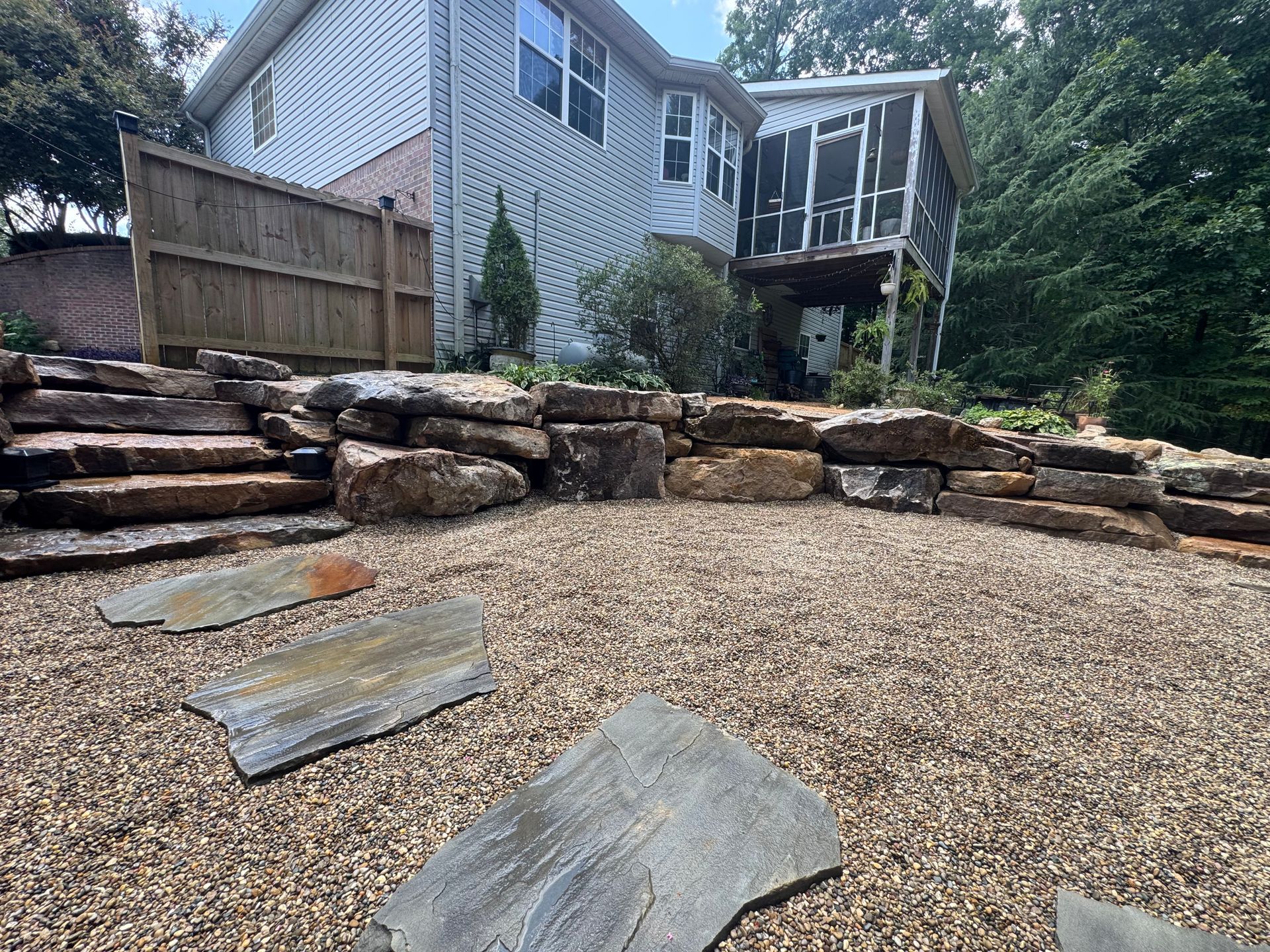 Backyard gravel patio with stone retaining wall, steps, and a house deck above the slope