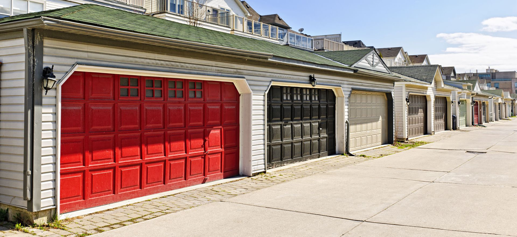 Row of garages with red, black, and gray doors. Green roofs and concrete pavement.