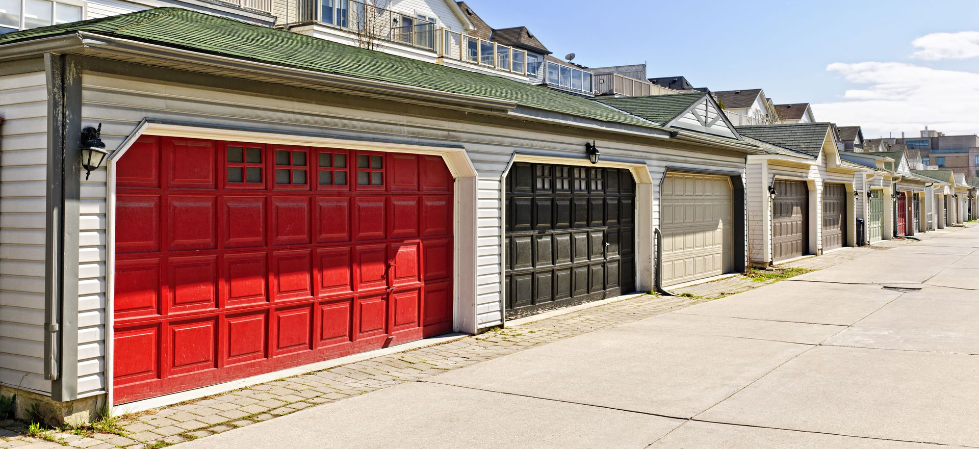 Row of garages with red, black, and gray doors. Green roofs and concrete pavement.