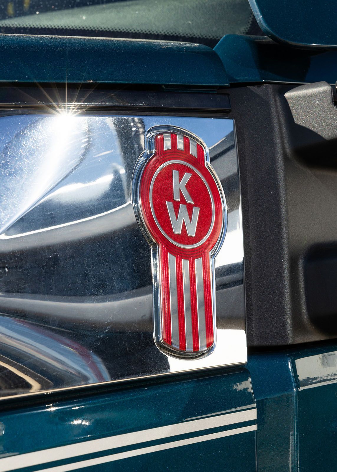 Kenworth truck logo on a teal cab with a chrome and red emblem