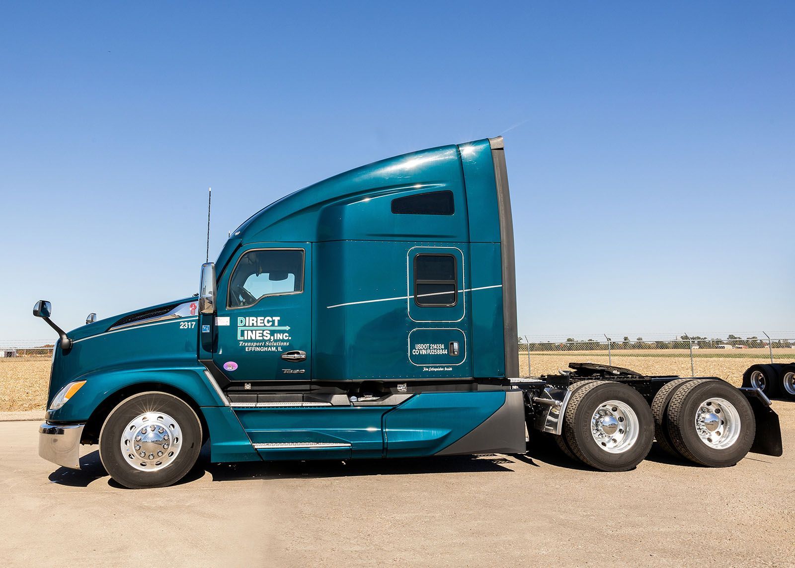 Teal semi-truck parked in front of a blue sky and dry landscape