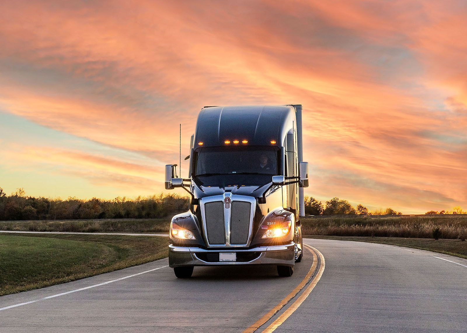 A semi-truck driving on a road with a vibrant orange and pink sunset in the background
