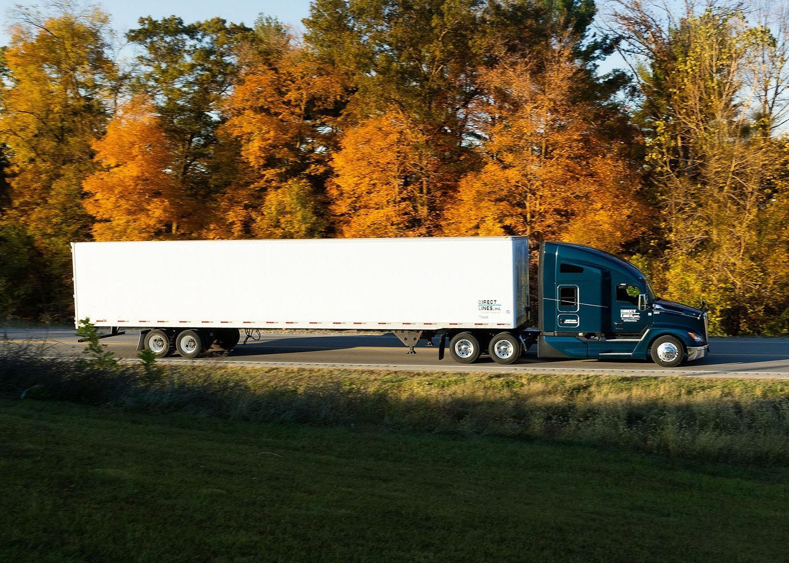Blue semi-truck driving on a road with a white trailer