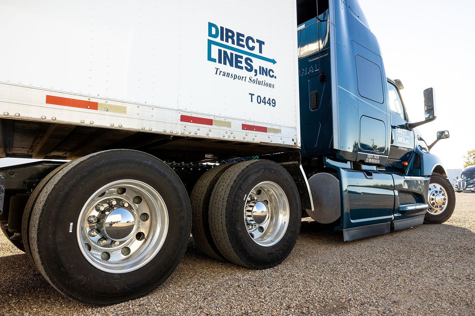 Semi-truck with a white trailer, parked on gravel
