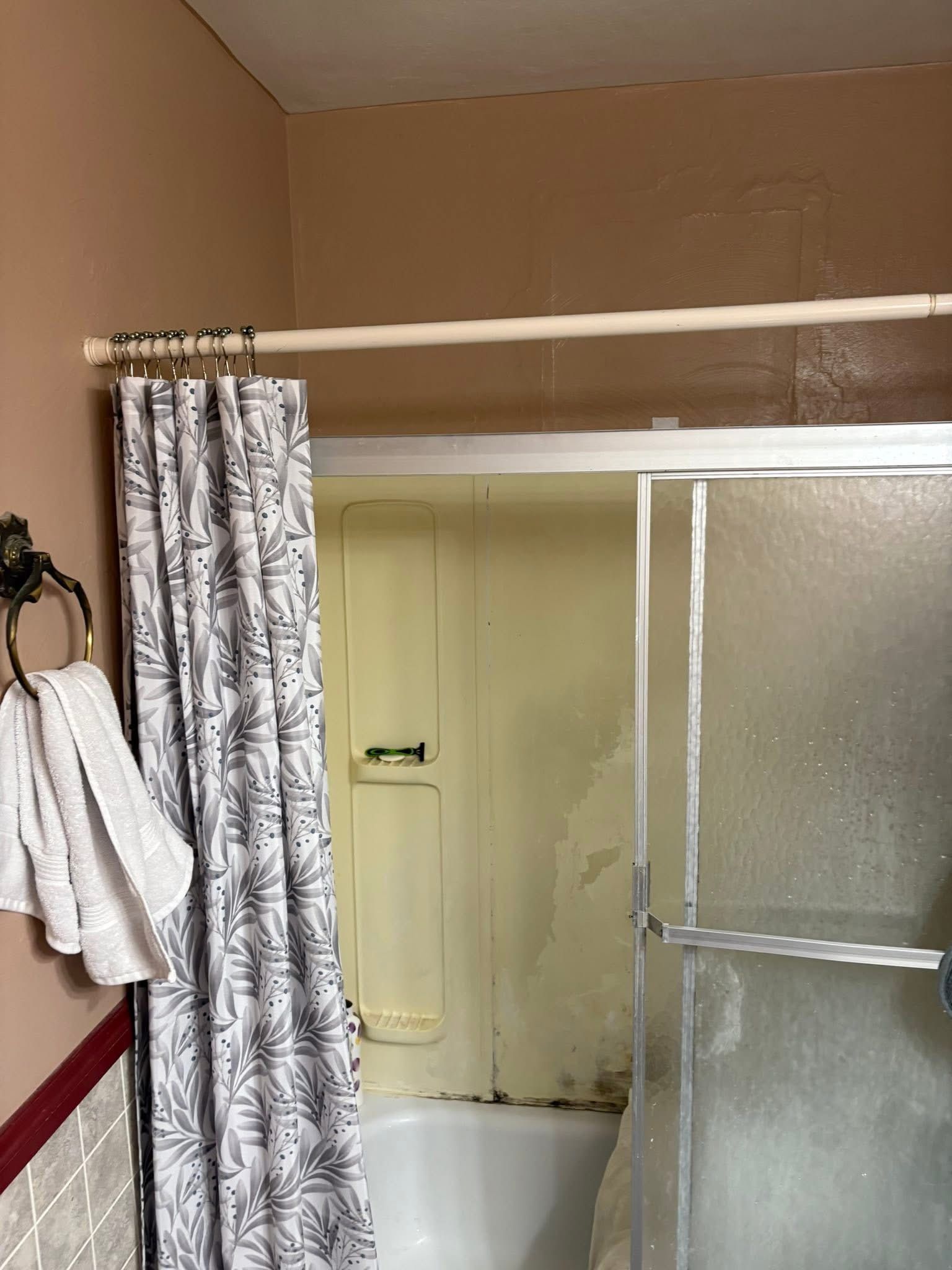 Bathroom with shower curtain, tub, and glass shower door. Beige walls. White towel.
