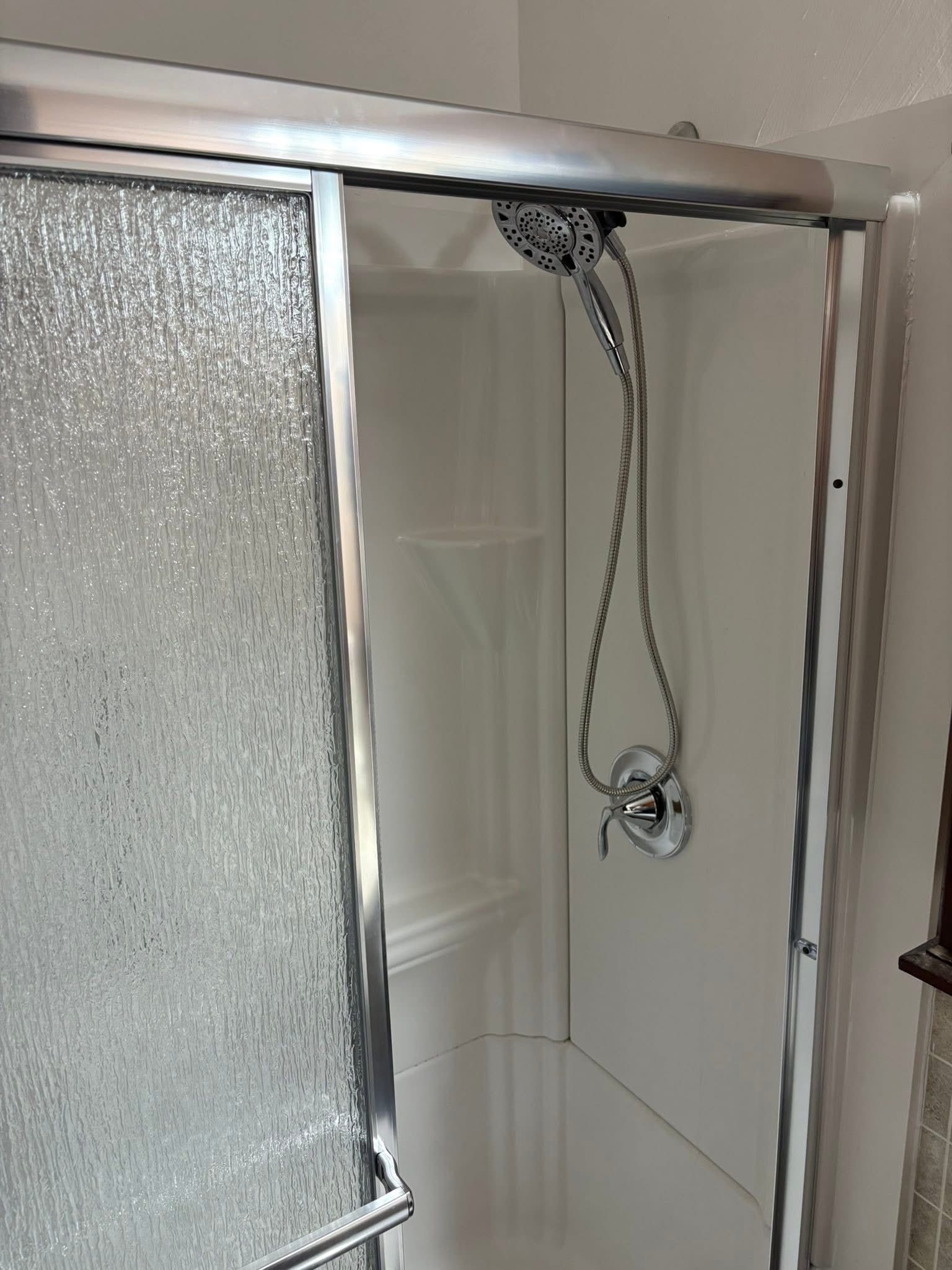 Shower with sliding frosted glass door, silver trim, and a handheld showerhead.