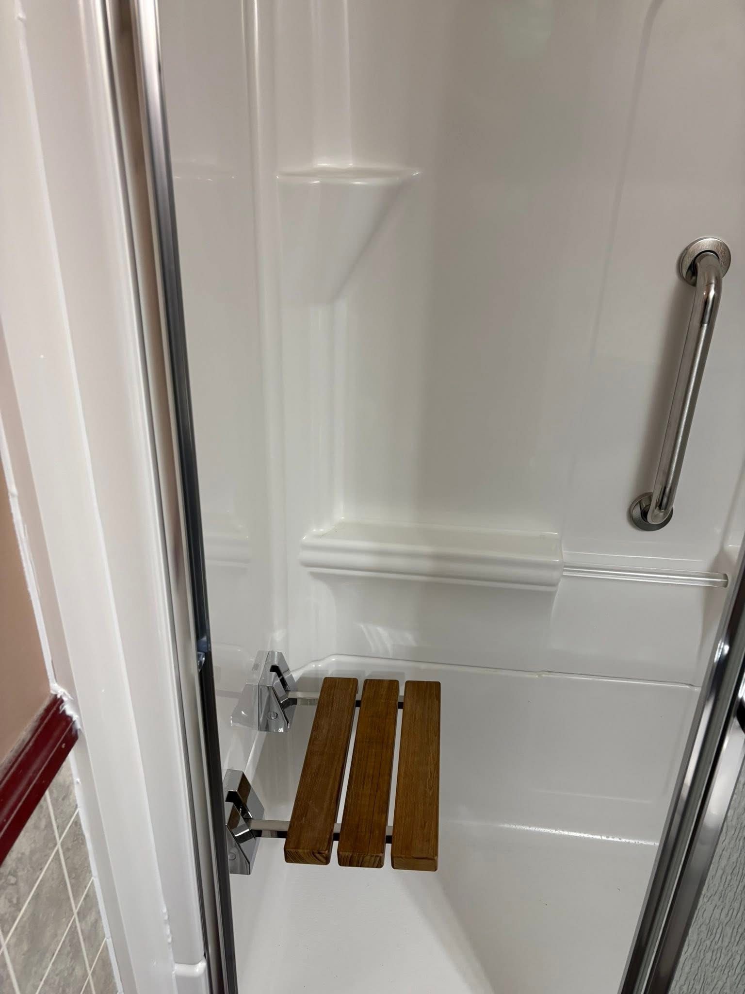 Shower stall with a wooden fold-down seat and grab bar for accessibility.