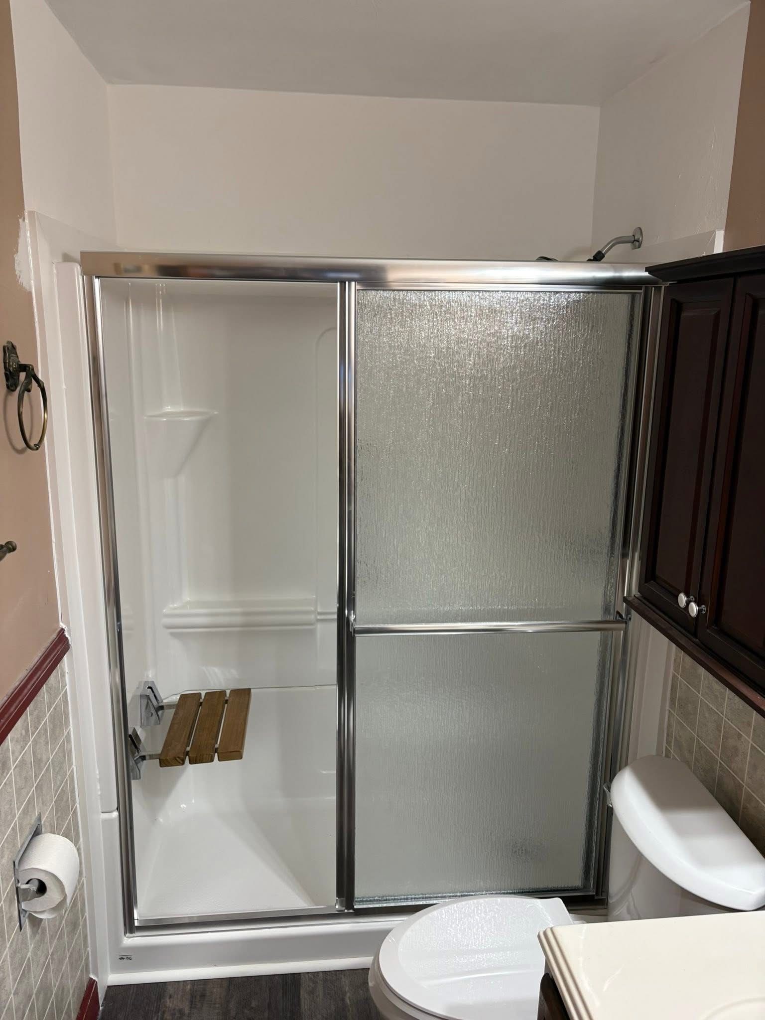 Shower stall with sliding glass doors, wooden seat, and toilet.