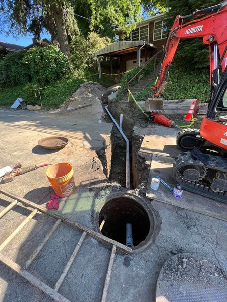 Construction site with an open sewer manhole, trench, and orange excavator.