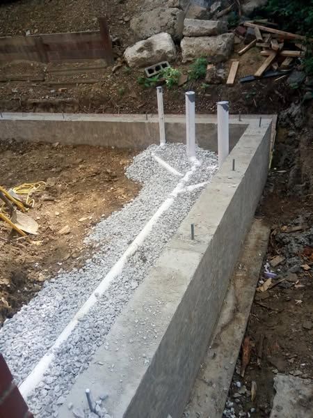 Concrete foundation with gravel and white pipes for construction.
