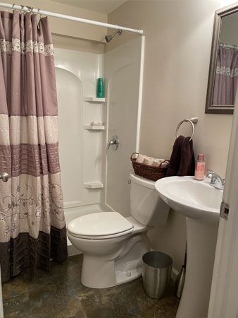 A small bathroom with a shower, toilet, and pedestal sink. Beige walls, brown and purple shower curtain.