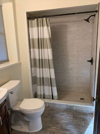 Bathroom with gray tile shower, toilet, striped shower curtain, and dark brown fixtures.