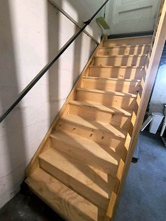 Wooden staircase with handrail, leading upward. Sunlight casts shadows on the steps.