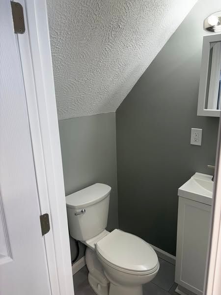 Small bathroom with a toilet and sink. Angled ceiling and gray walls.