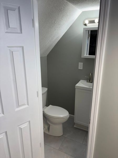 Small bathroom with a toilet, sink, and slanted ceiling. Gray walls and white fixtures.