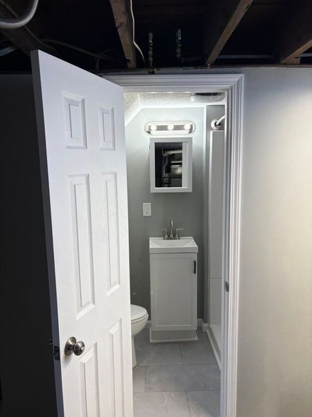 Bathroom interior with white door, vanity, and shower. Gray walls and tile floor.