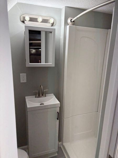 Small, gray-walled bathroom with white vanity, shower, and medicine cabinet. Chrome fixtures.