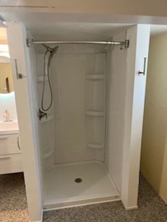 White shower stall with shelves, chrome fixtures, and a shower rod in a bathroom.